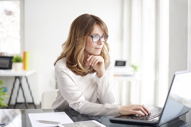 woman smiles slightly while typing on laptop